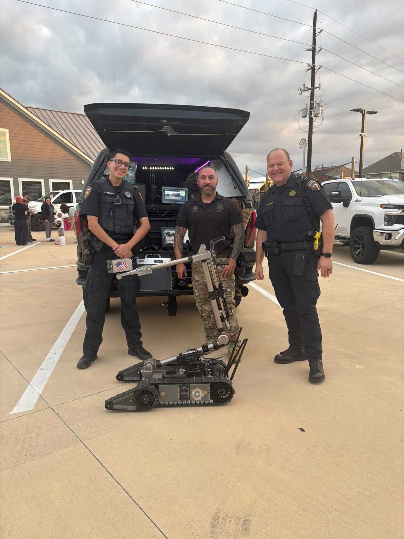 Public safety personnel stand with a tracked bomb disposal robot in front of a law enforcement vehicle displaying specialized equipment during a community safety event.