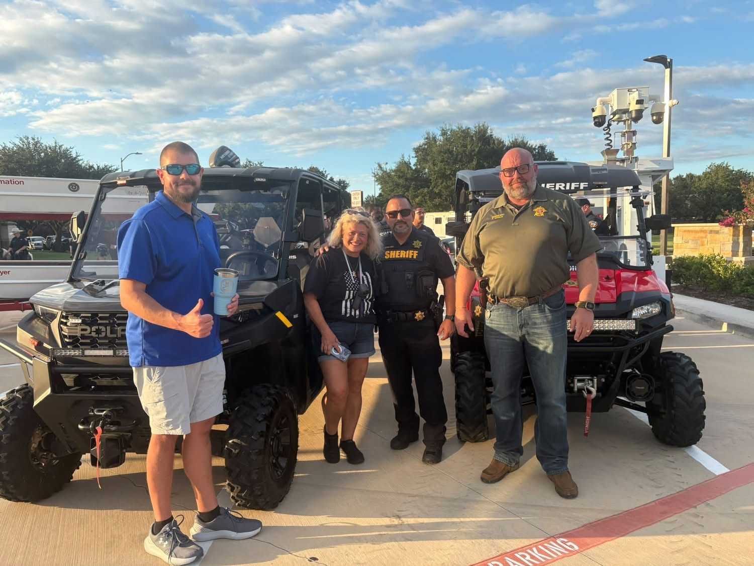 Community members and sheriff’s deputies pose beside off-road utility vehicles at an outdoor public safety event in a parking lot, with law enforcement equipment and emergency response vehicles visible.